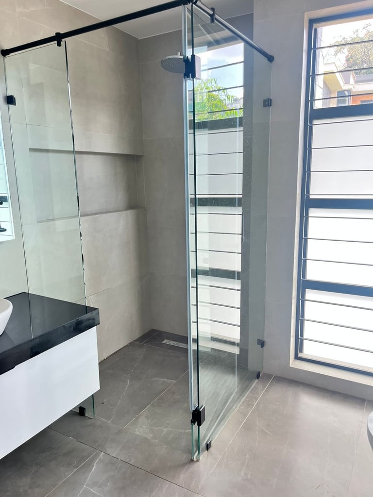 Modern bathroom with frameless glass shower enclosure, gray tile walls and flooring, white vanity, and louvered window