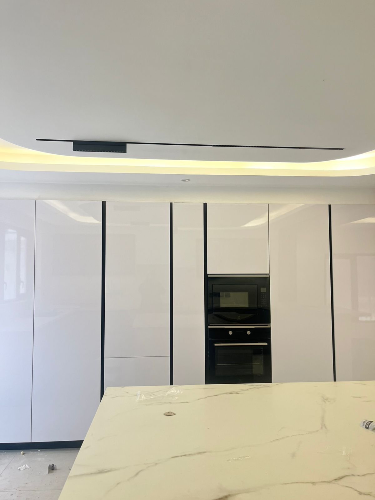 Modern kitchen under renovation with white cabinetry, black built-in oven, marble countertop, and curved ceiling with LED lighting