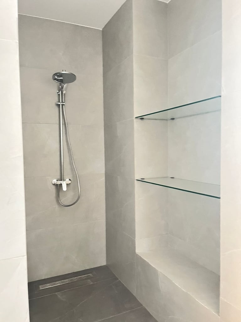 Modern shower stall with rainfall showerhead, chrome fixtures, grey tile walls, and glass shelves for storage