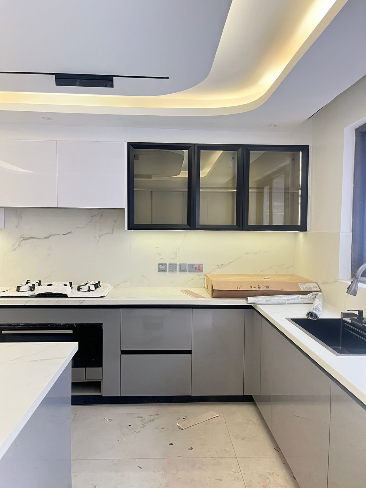 Modern kitchen with white cabinetry, marble backsplash, black-framed window cabinets, gas cooktop, and curved ceiling lights