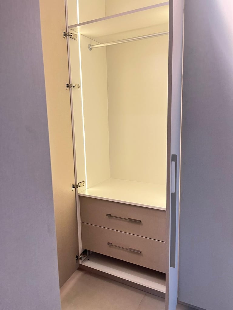 Empty built-in wardrobe with glass doors, interior shelving, hanging rod, and two wooden drawers below