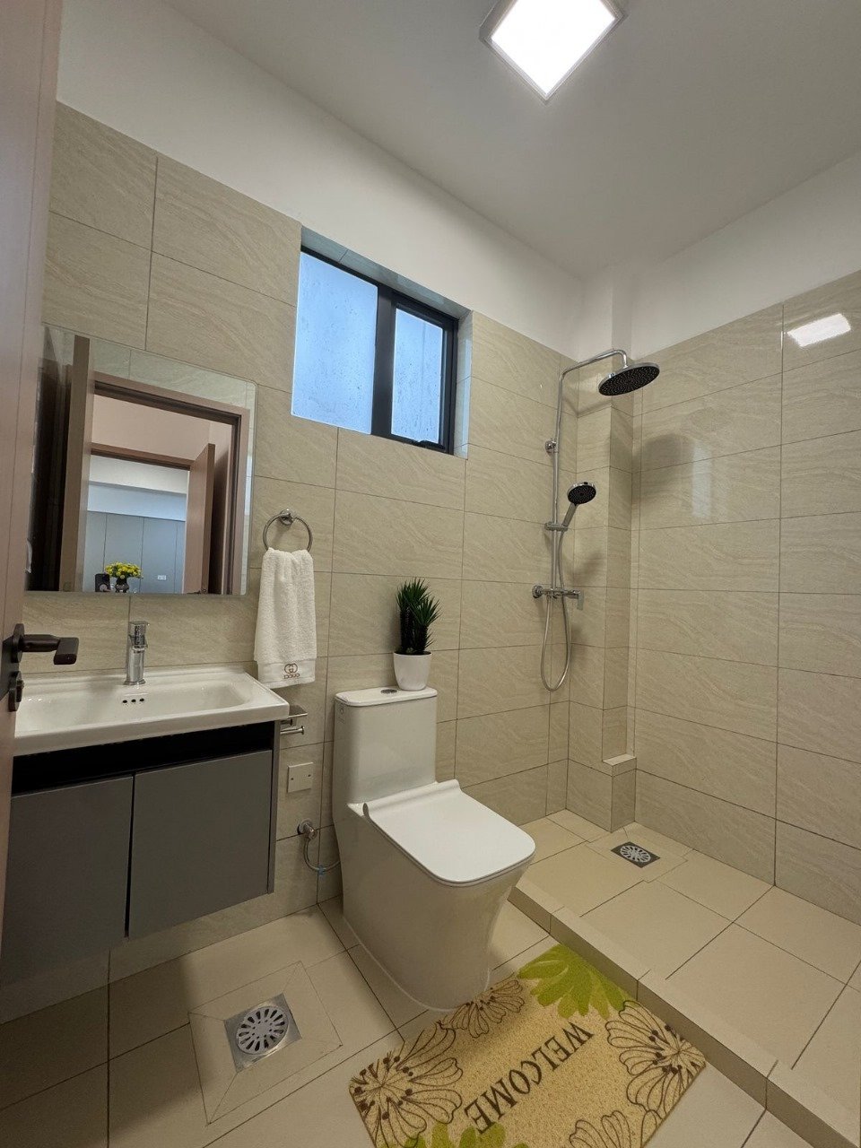 Modern bathroom with beige tile walls, floating sink vanity, toilet, and walk-in shower with black fixtures and small window