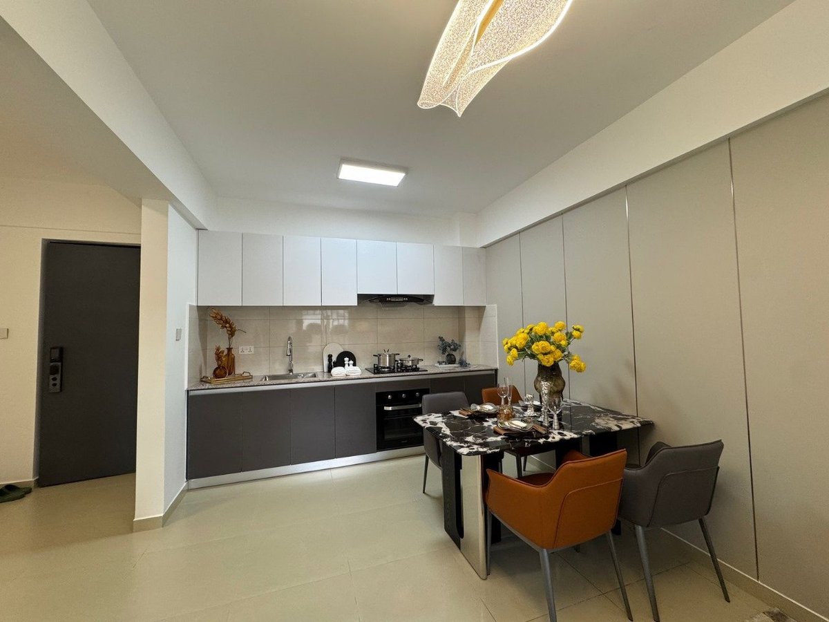 Modern open-plan kitchen and dining area with black cabinetry, dining table with orange and gray chairs, and yellow flowers in a vase