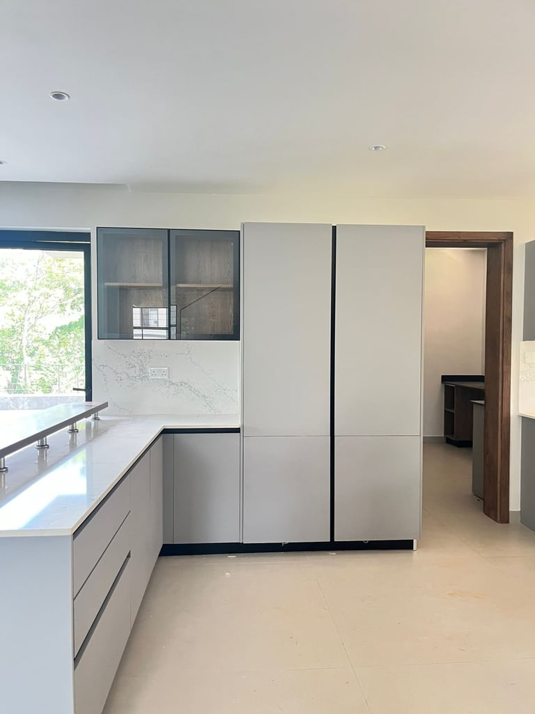 Modern kitchen interior with white cabinets, large window, and stainless steel refrigerator in an open floor plan