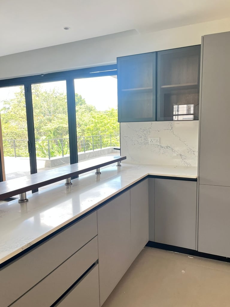 Modern minimalist kitchen with white cabinetry, blue glass upper cabinets, and large windows overlooking greenery