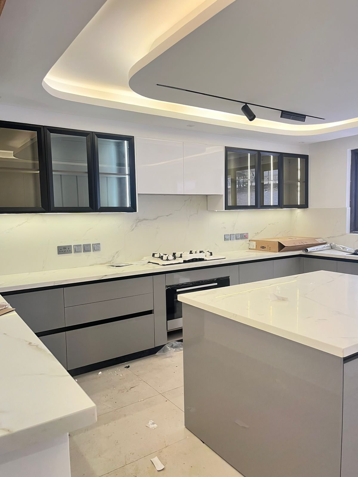 Modern kitchen with white and gray cabinetry, white marble countertops, island, and curved ceiling lighting