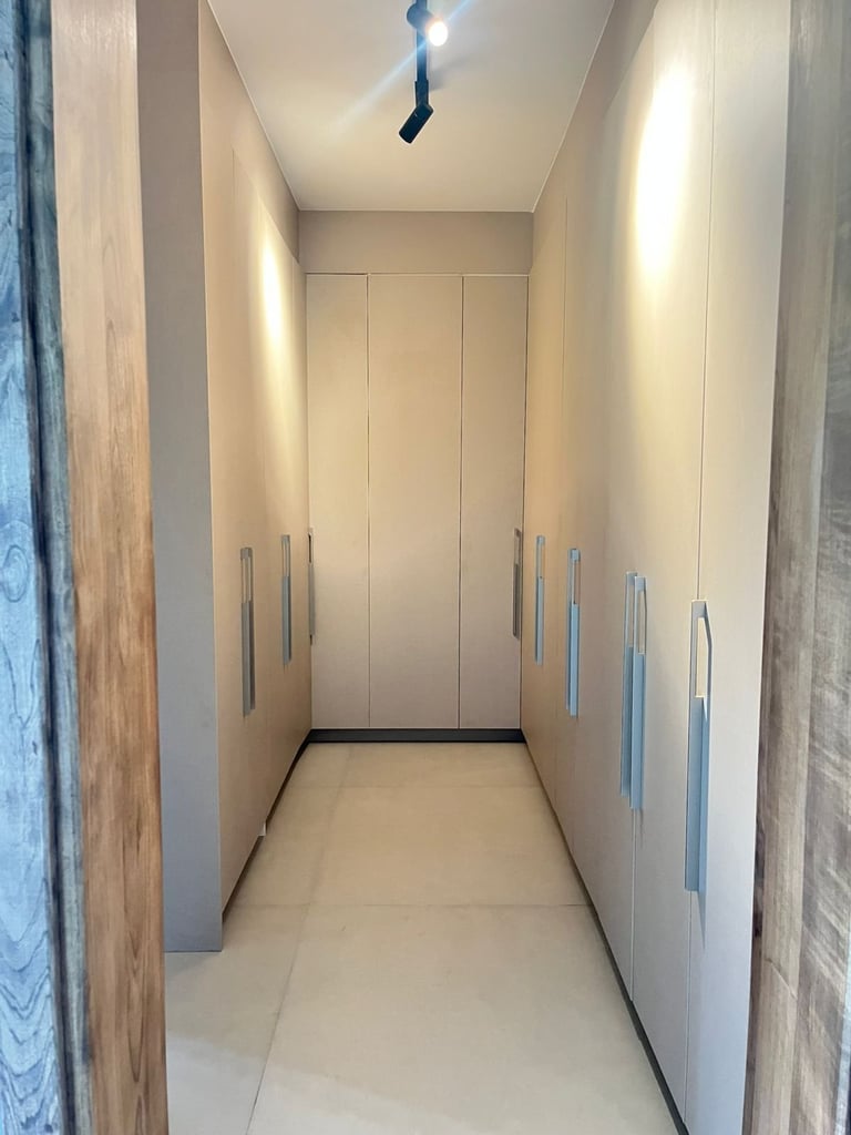 Modern narrow hallway with beige walls, recessed lighting, and built-in storage cabinets with metal handles on both sides