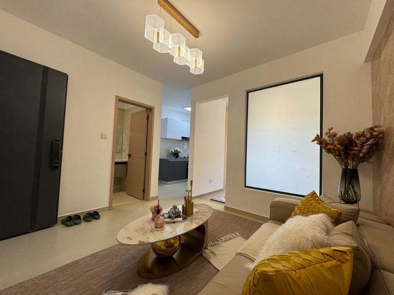 Modern apartment living room with sofa, coffee table, and kitchen visible in the background under a modern ceiling fixture