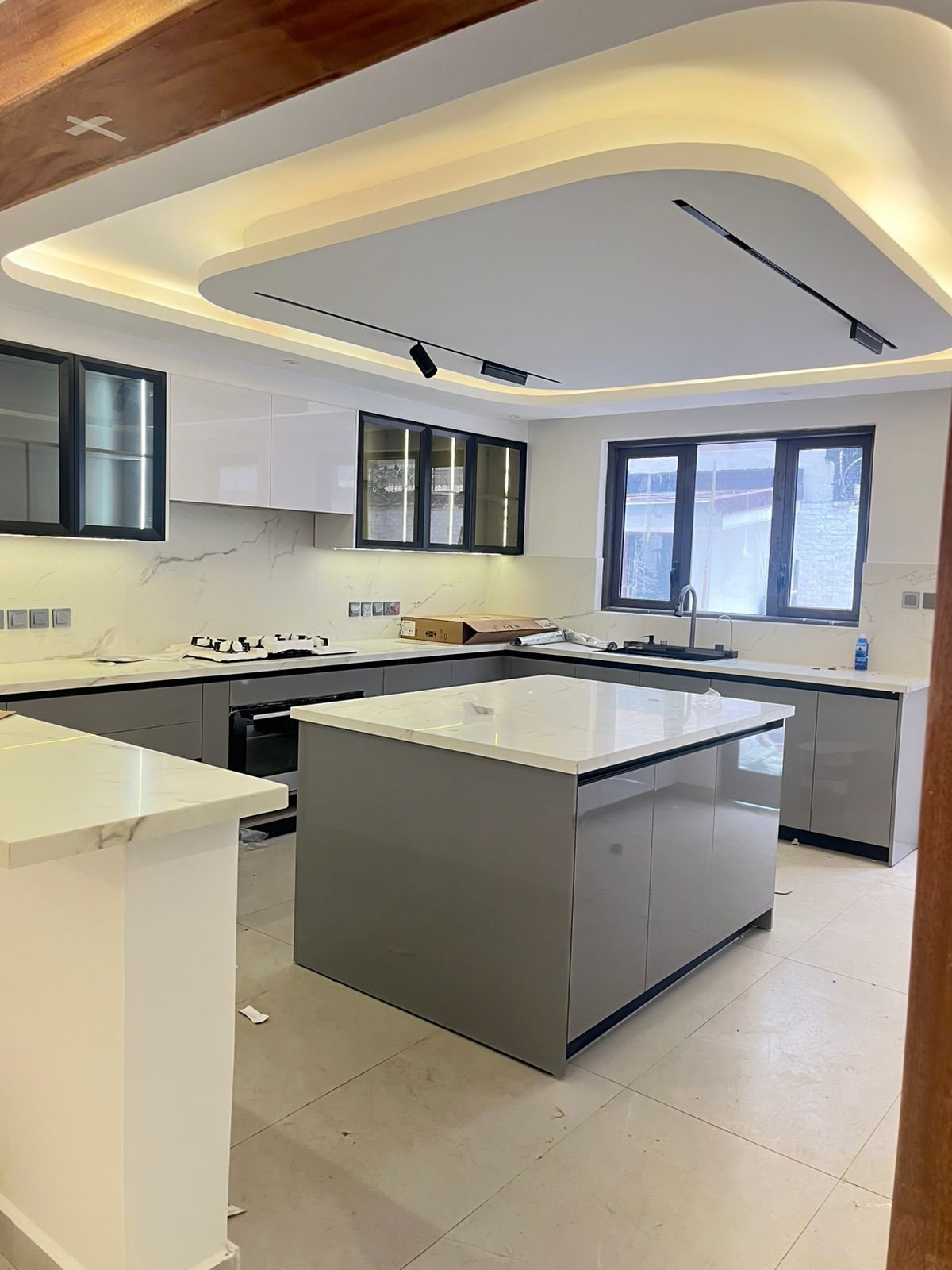 Modern kitchen with white and gray cabinetry, central island, stainless steel appliances, and curved ceiling with ambient lighting