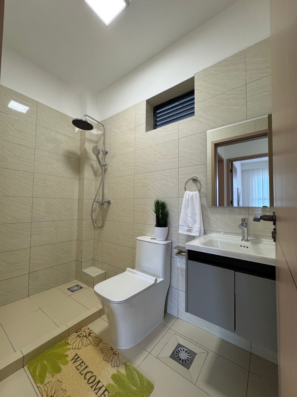 Modern bathroom interior with light green tile walls, white toilet, dark vanity with sink, mirror, and walk-in shower